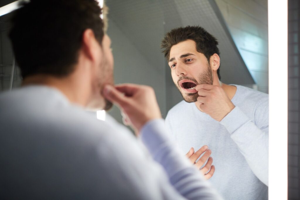 man checking teeth in mirror